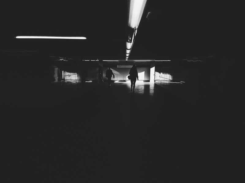 Silhouetted people walking through a dark concrete underpass towards a bright opening.