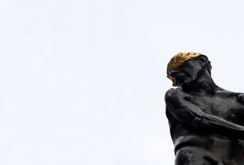 A dark, laurel-crowned statue against a pale sky.