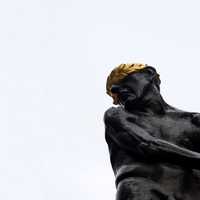 A dark, laurel-crowned statue against a pale sky.