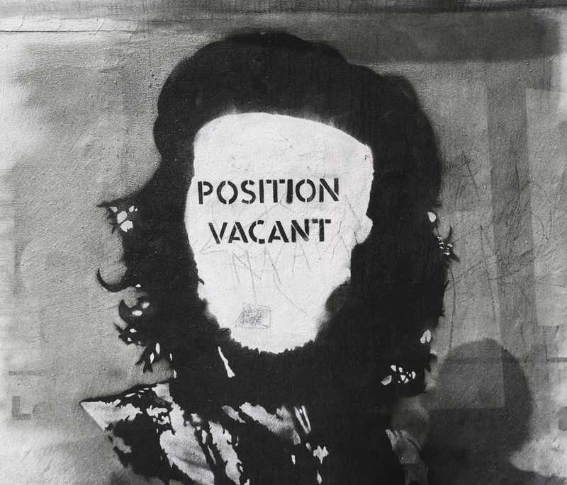 A black-and-white stencil portrait on a wall with the words 'POSITION VACANT' across the face.